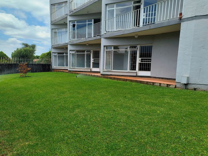 Rear view of a multi-story townhouse complex featuring a shared lawn, paved patio areas, and metal balcony railings.