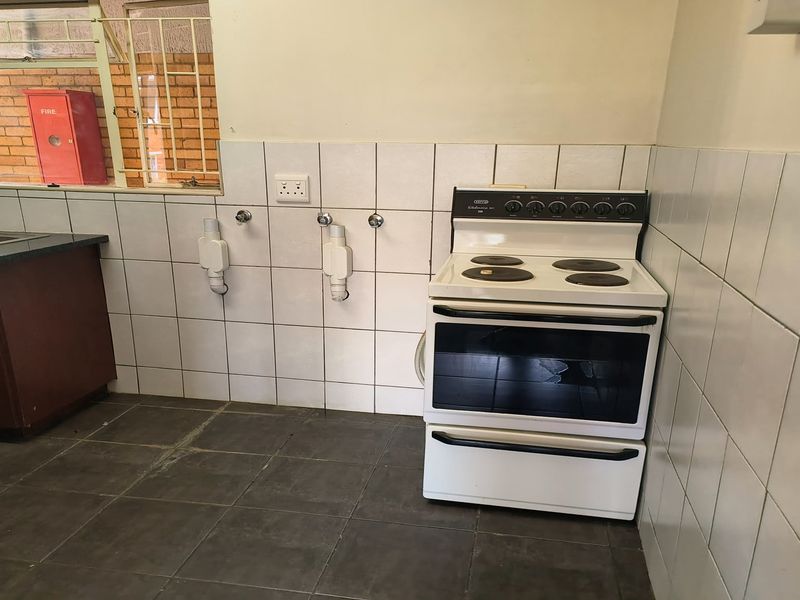 A functional kitchen area featuring a freestanding electric stove, tiled splashbacks, and a double sink unit with dark countertops.
