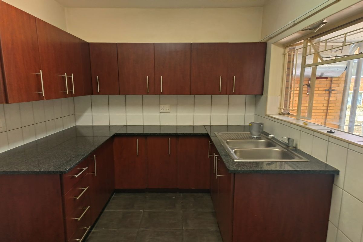 A functional kitchen featuring dark wood cabinetry, granite countertops, a double-basin stainless steel sink, and tiled splashbacks with a large window for natural light.
