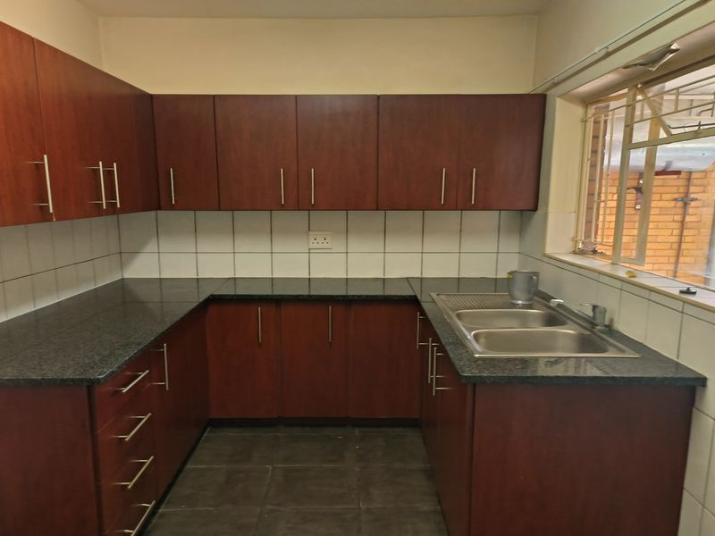 A functional kitchen featuring dark wood cabinetry, granite countertops, a double-basin stainless steel sink, and tiled splashbacks with a large window for natural light.