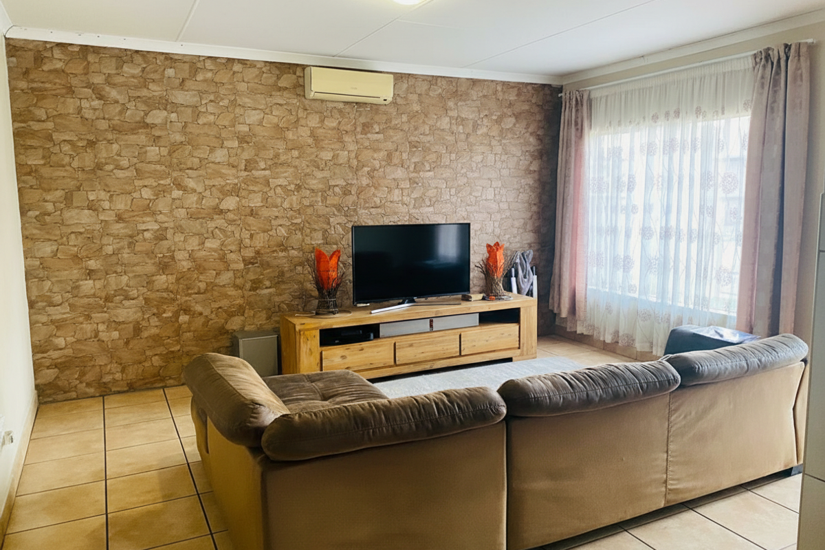 A comfortable living room featuring tiled flooring, a stone-look feature wall, and a wall-mounted air conditioning unit.
