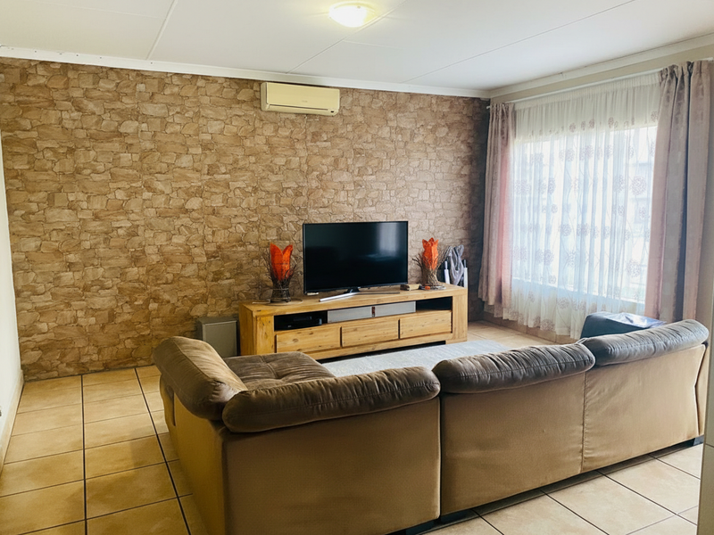 A comfortable living room featuring tiled flooring, a stone-look feature wall, and a wall-mounted air conditioning unit.