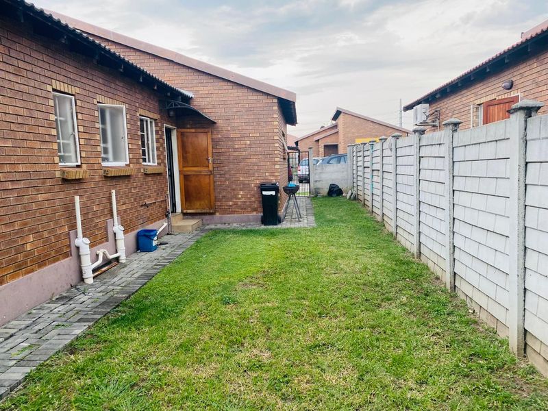 A view of the rear exterior of the house featuring a face brick facade, a small lawn area, and a precast concrete boundary wall.
