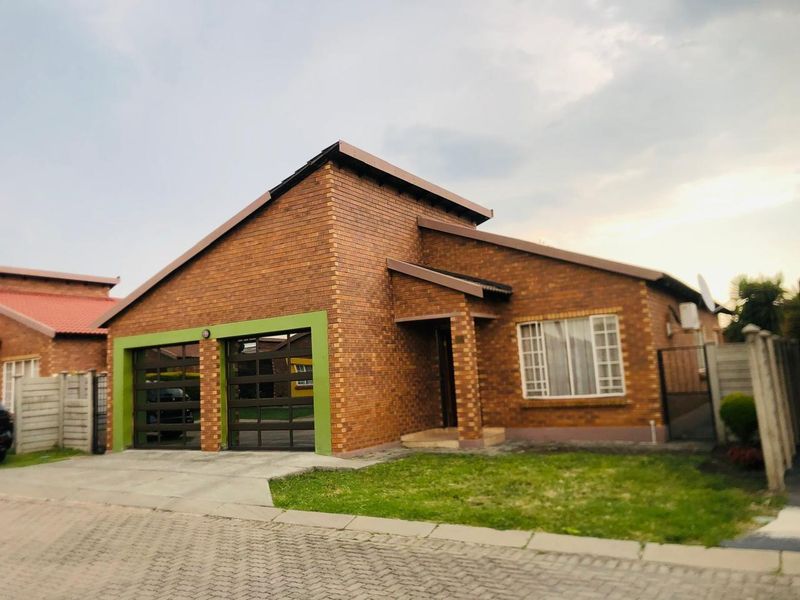 Front view of a face-brick residential house featuring a double garage with modern doors, a paved driveway, and a small front garden area.