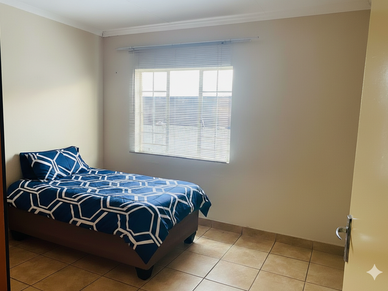 A simple bedroom featuring neutral wall tones, tiled flooring, and a window fitted with venetian blinds.