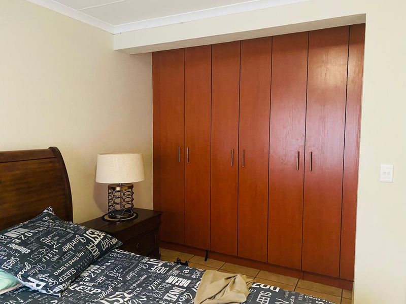 A bedroom featuring floor-to-ceiling built-in wooden cupboards and tiled flooring.