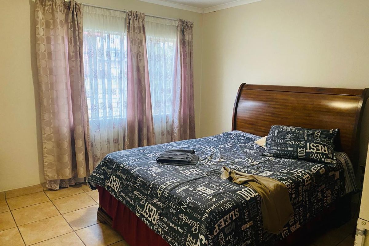 A functional bedroom featuring tiled flooring and natural light through a window with installed curtain rails.