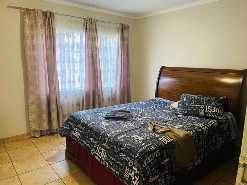 A functional bedroom featuring tiled flooring and natural light through a window with installed curtain rails.