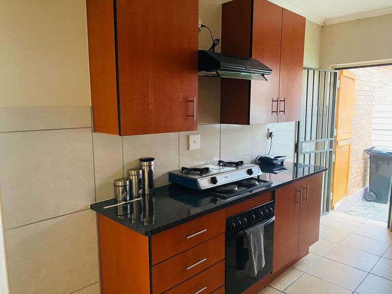 Compact kitchen featuring wooden cabinetry, granite countertops, built-in oven, gas hob, and extractor fan, with direct access to an exterior area.