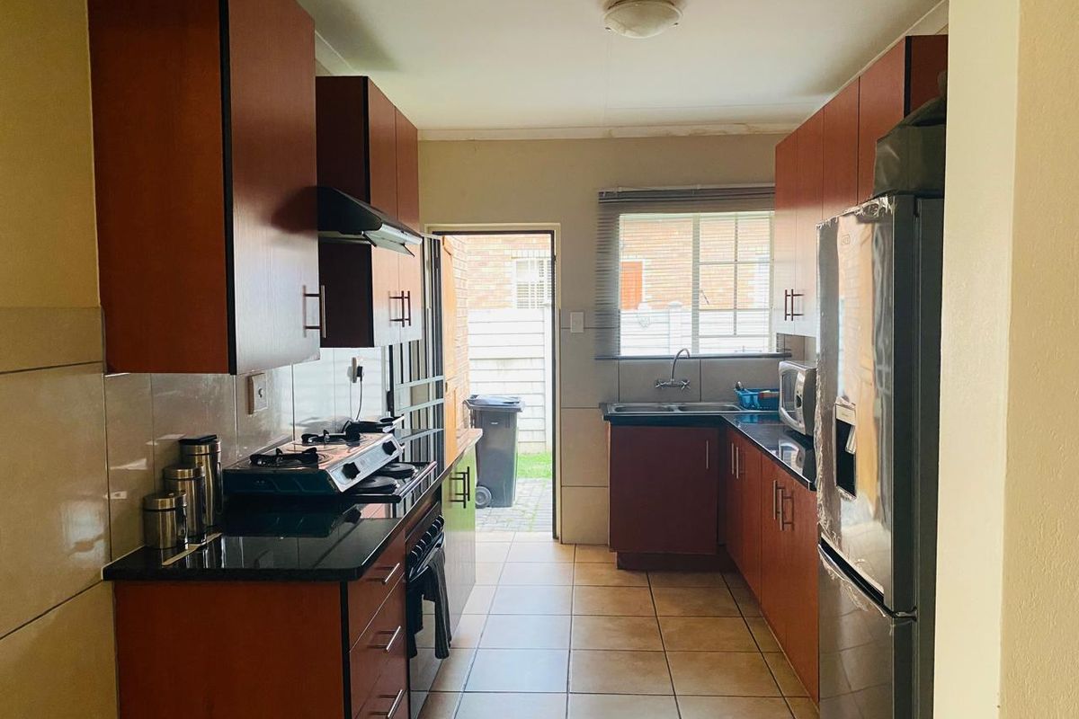 Functional galley-style kitchen featuring dark wood cabinetry, granite countertops, gas hob, extractor fan, and tiled flooring with direct access to the rear exterior.
