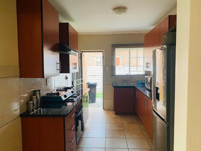 Functional galley-style kitchen featuring dark wood cabinetry, granite countertops, gas hob, extractor fan, and tiled flooring with direct access to the rear exterior.