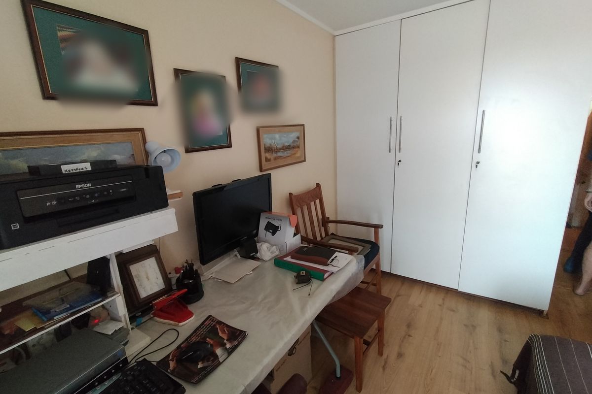 A bedroom featuring light-toned laminate flooring and a large, white built-in wardrobe with vertical handles.