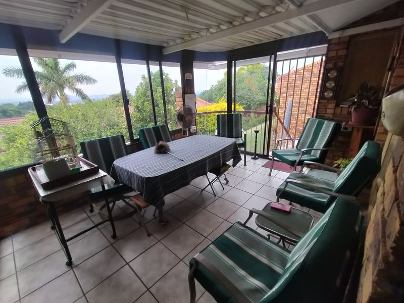 A covered patio area featuring tiled flooring, brick walling, and large sliding glass doors that provide views of the surrounding garden and landscape.