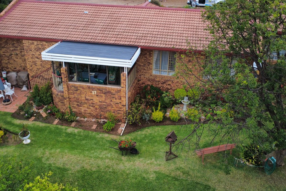 Aerial view of the rear elevation featuring a face brick facade, tiled roof, and an enclosed patio overlooking a well-maintained garden.