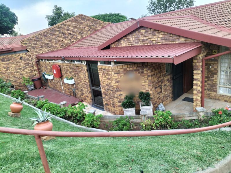 A view of the rear exterior of the retirement village unit, featuring face brick construction, a tiled roof, and a well-maintained garden area.