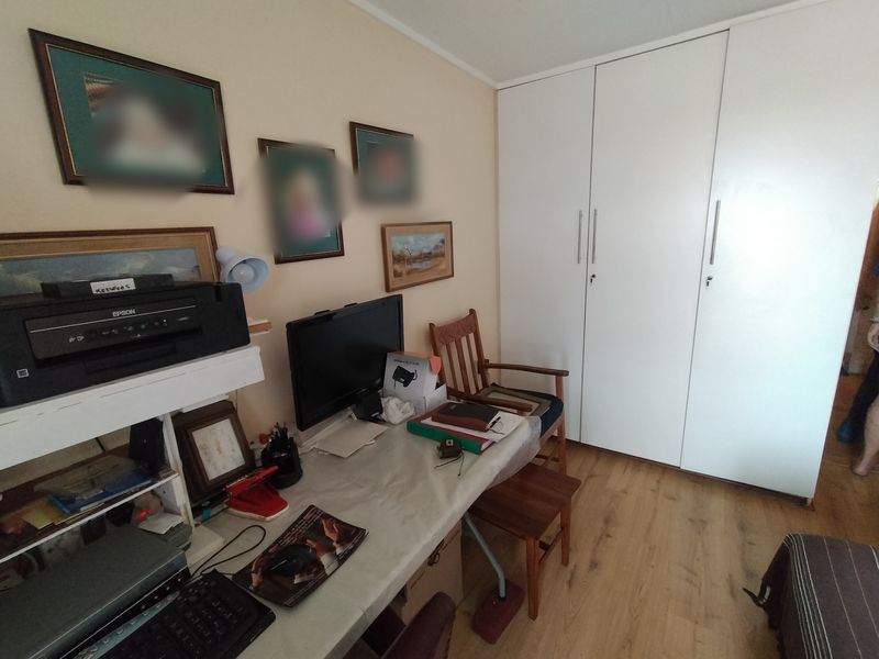 A bedroom featuring light-toned laminate flooring and a large white built-in wardrobe with modern handles.