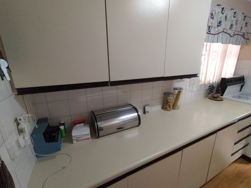 A functional kitchen area featuring laminate countertops, built-in cabinetry, and ceramic wall tiling, providing a practical workspace for daily meal preparation.
