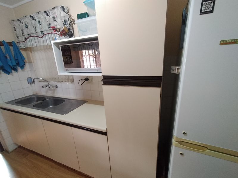 A functional kitchen area featuring laminate countertops, a double bowl stainless steel sink, tiled splashback, and built-in cabinetry with integrated microwave housing.