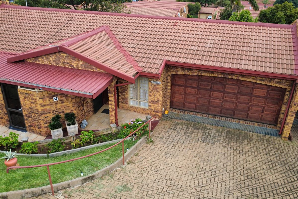 Aerial view of a brick retirement village unit featuring a tiled roof, double garage, and a paved driveway with landscaped garden borders.