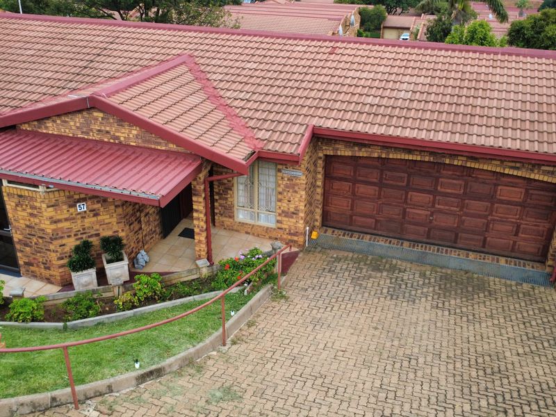 Aerial view of a brick retirement village unit featuring a tiled roof, double garage, and a paved driveway with landscaped garden borders.