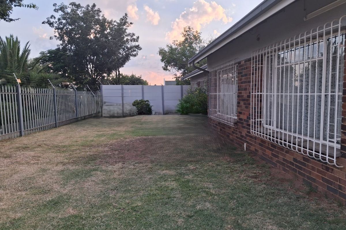 A view of the rear garden featuring a brick exterior wall with security bars and perimeter fencing.
