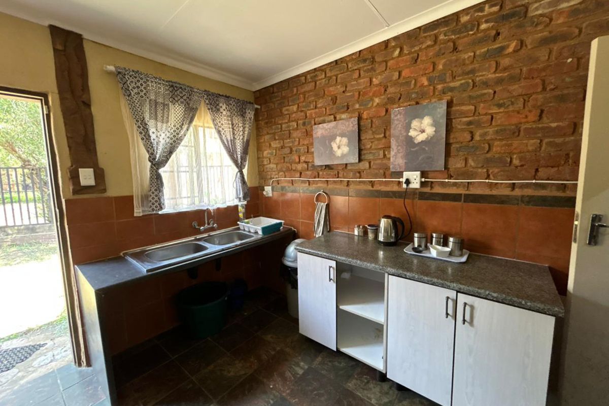A rustic kitchen area featuring exposed brick walls, a double basin sink, tiled splashbacks, and functional base cabinetry with laminate countertops.