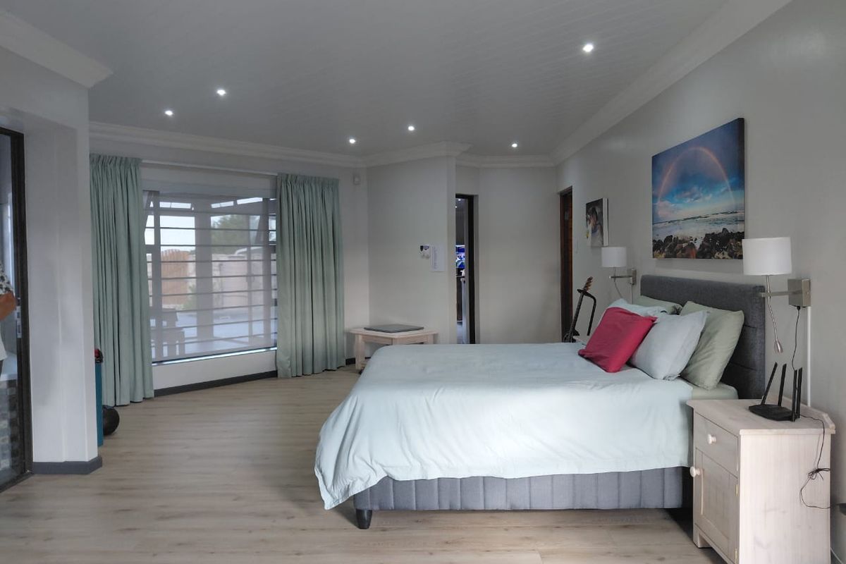 Spacious bedroom featuring modern laminate flooring, recessed downlighting, and large windows with curtains, offering a bright and comfortable living space.