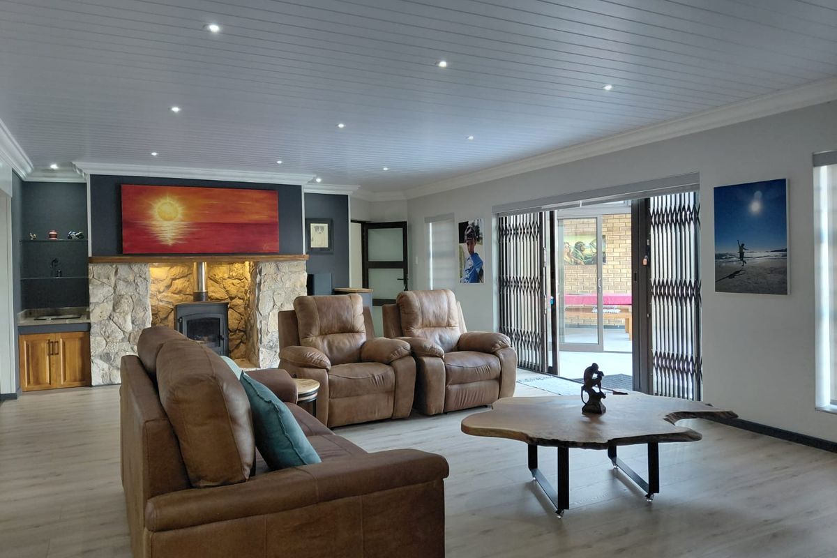 Spacious living room featuring a stone fireplace with a wood-burning stove, recessed lighting, laminate flooring, and sliding doors leading to an outdoor area.