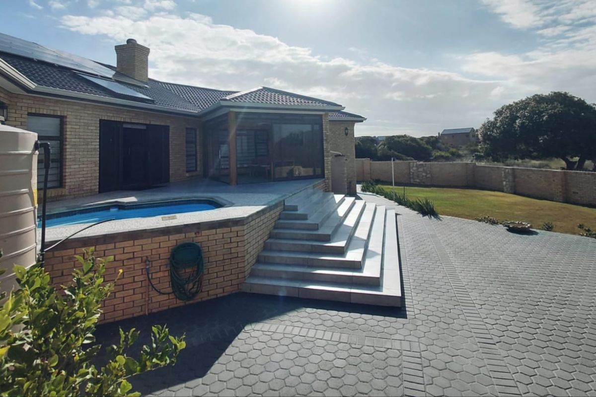 Rear exterior view featuring a paved patio area, swimming pool, brick facade, and a well-maintained garden with boundary walling.