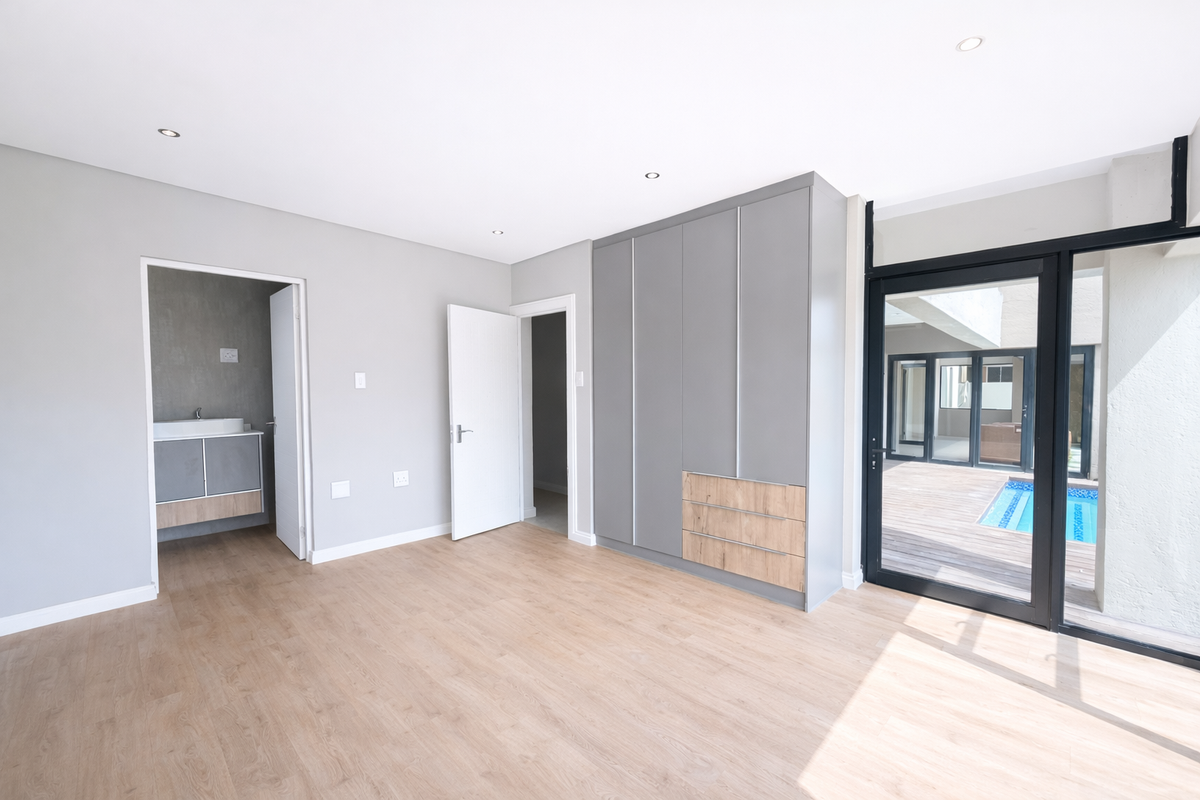Modern bedroom featuring light wood-look flooring, built-in grey cabinetry, recessed lighting, and direct access to a private patio with a swimming pool.
