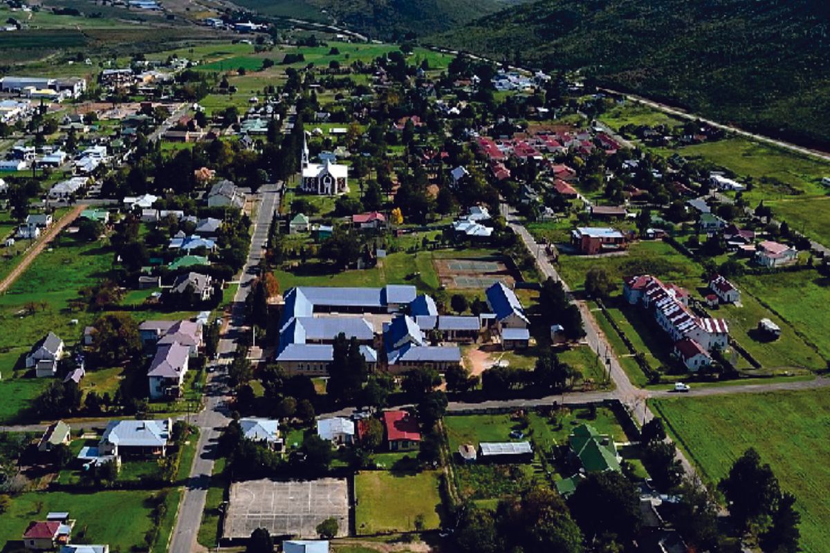An aerial view of a residential town featuring established housing, a church, and recreational facilities set against a mountainous landscape.
