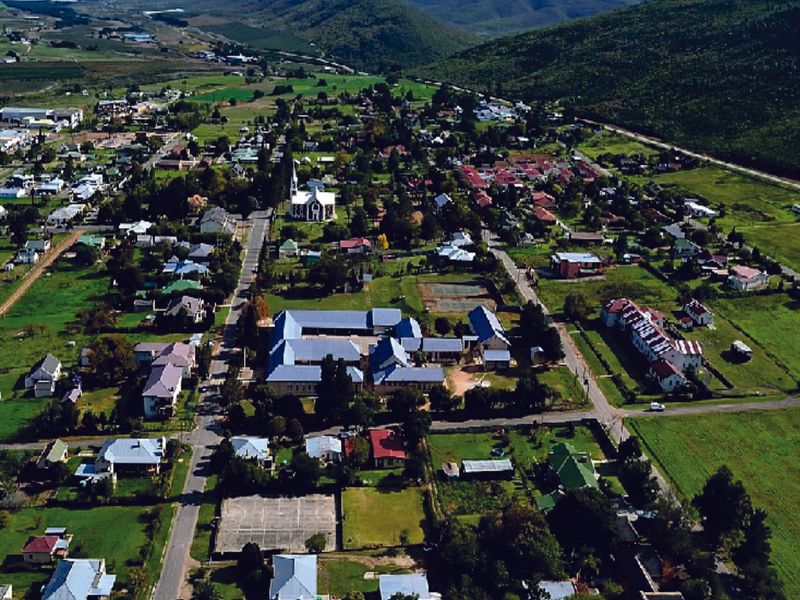 An aerial view of a residential town featuring established housing, a church, and recreational facilities set against a mountainous landscape.