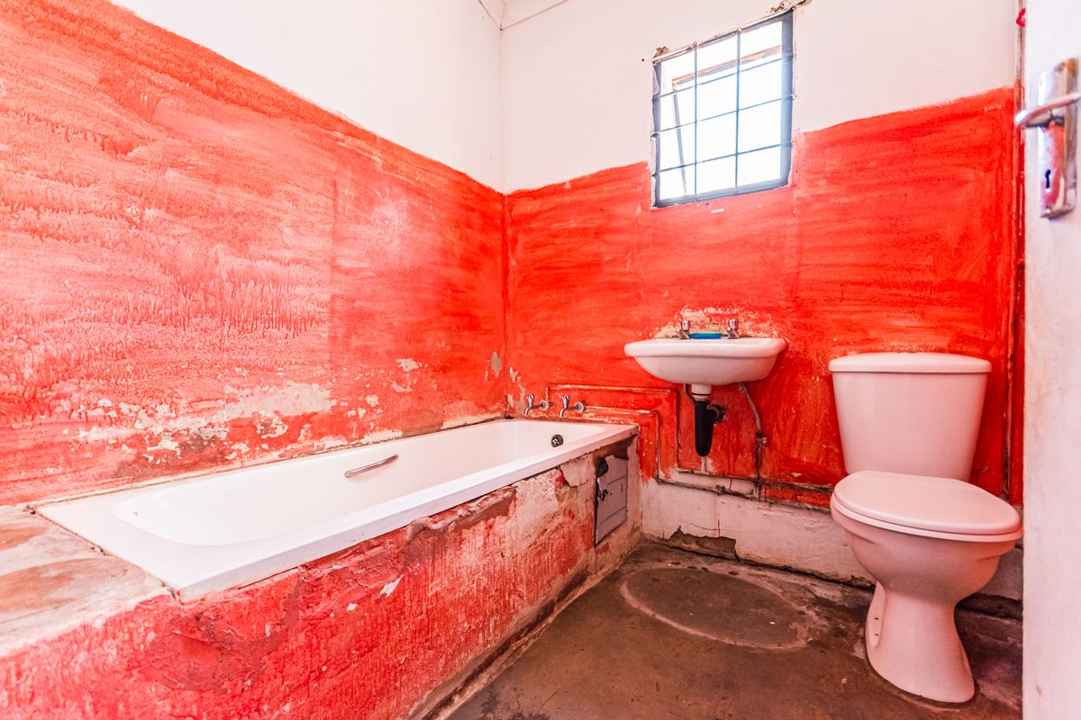 A bathroom in need of significant renovation, featuring a bathtub, wall-mounted basin, and toilet with severely damaged wall finishes.