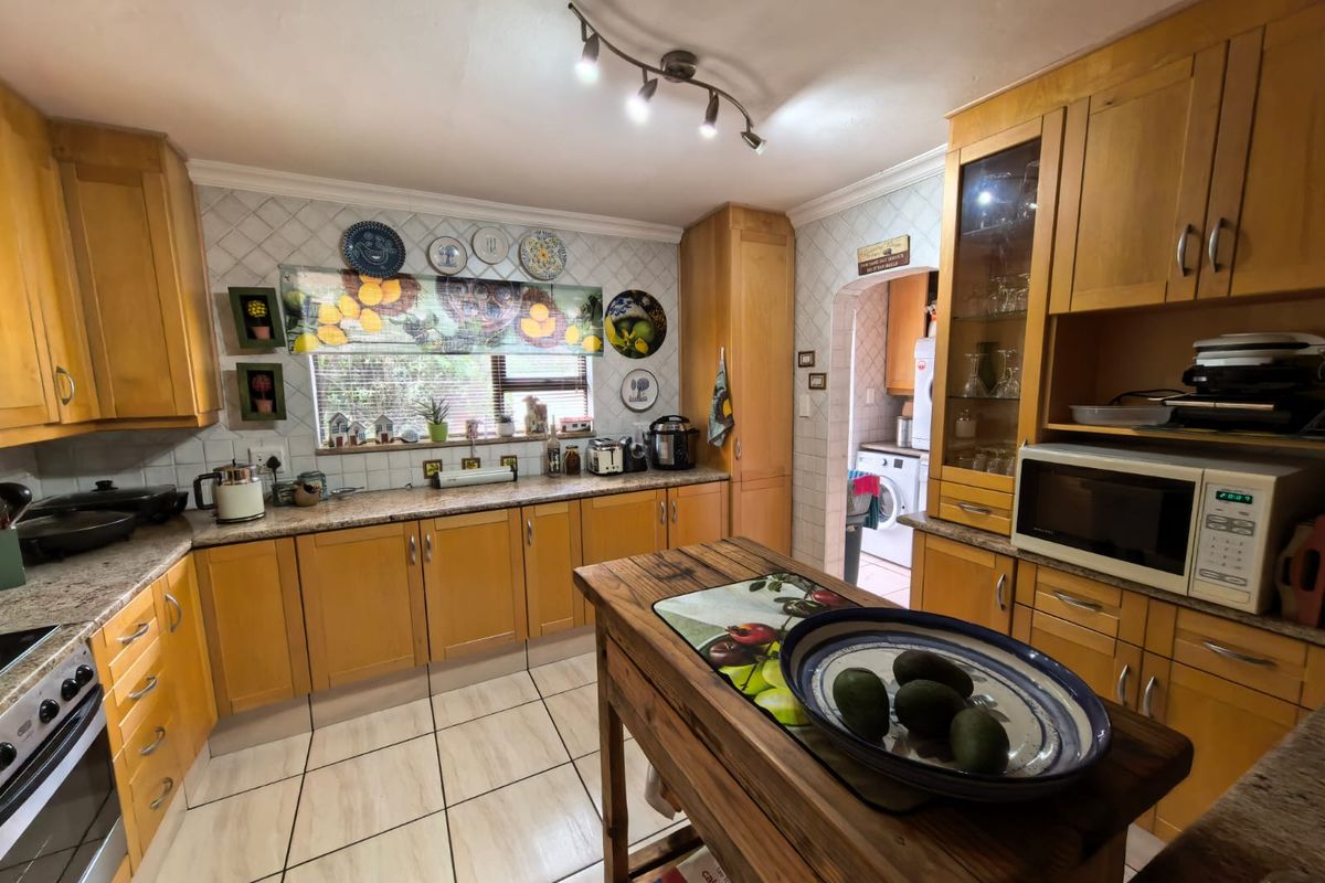 A functional kitchen featuring wooden cabinetry, granite countertops, tiled backsplash, and ceramic flooring, with an adjacent scullery area visible.