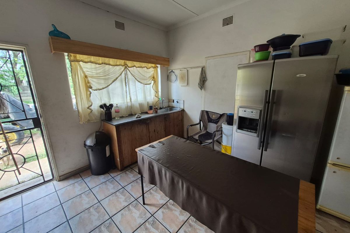 A dated kitchen area featuring basic cabinetry, a stainless steel sink, and tiled flooring with direct access to the exterior.