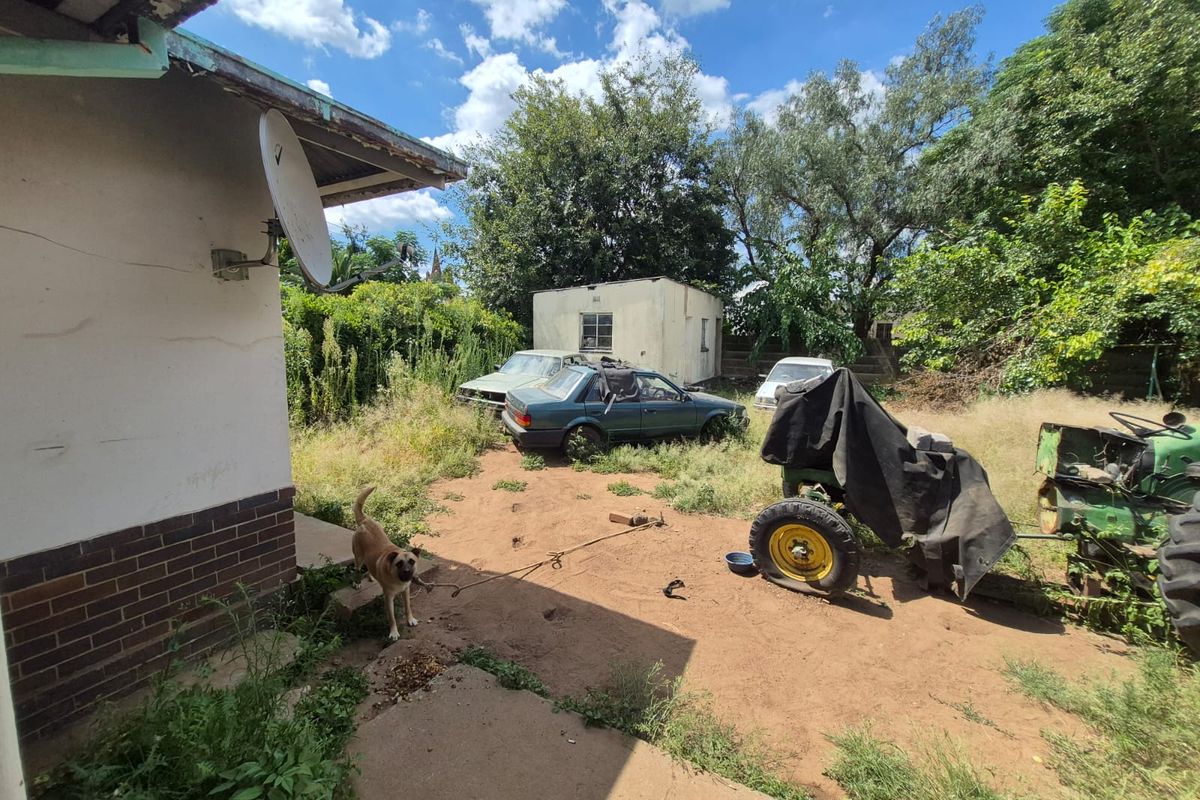 Rear exterior view of the property showing a large, unmaintained garden area with a detached outbuilding and significant overgrown vegetation.