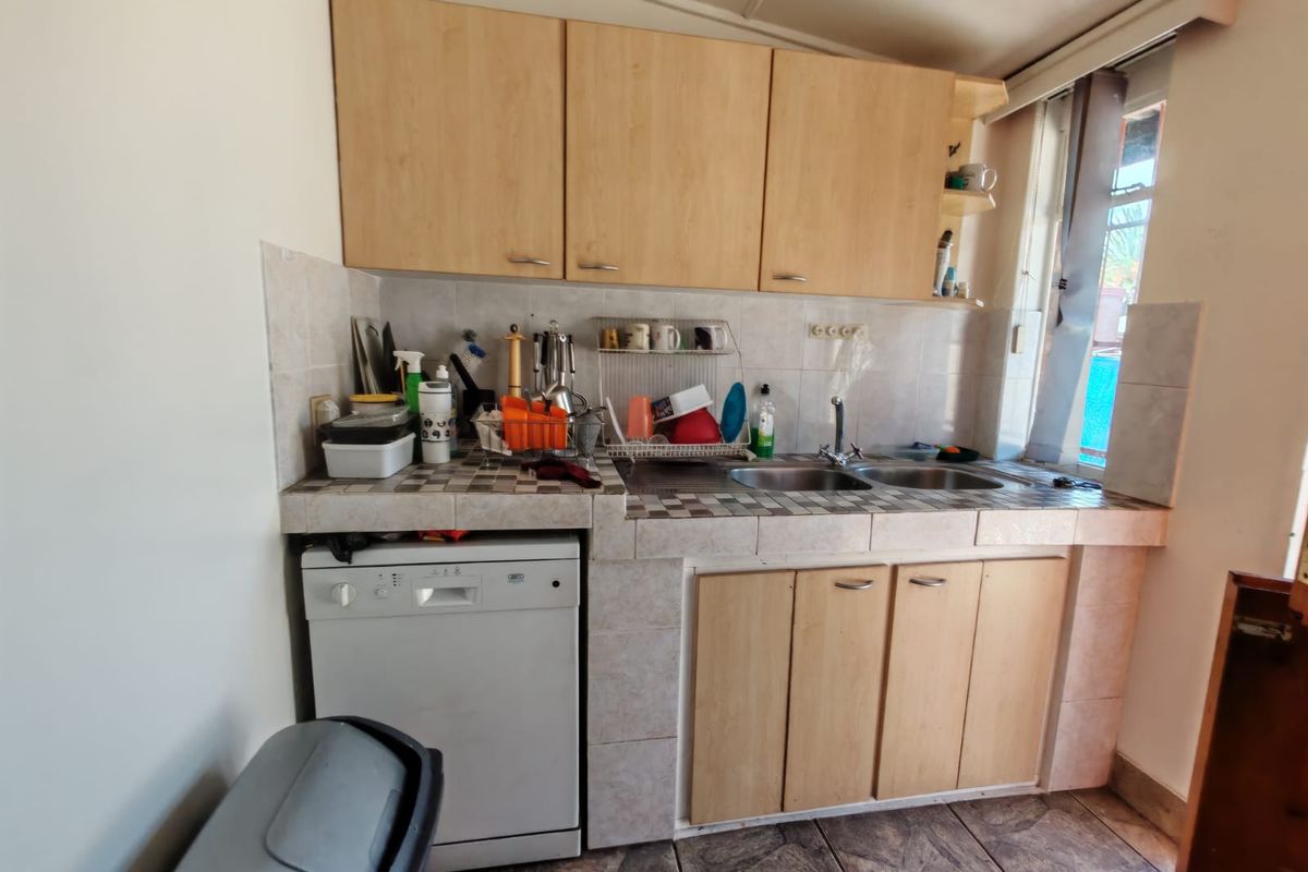 A compact kitchen featuring laminate cabinetry, a tiled countertop with a double basin sink, and a built-in dishwasher.