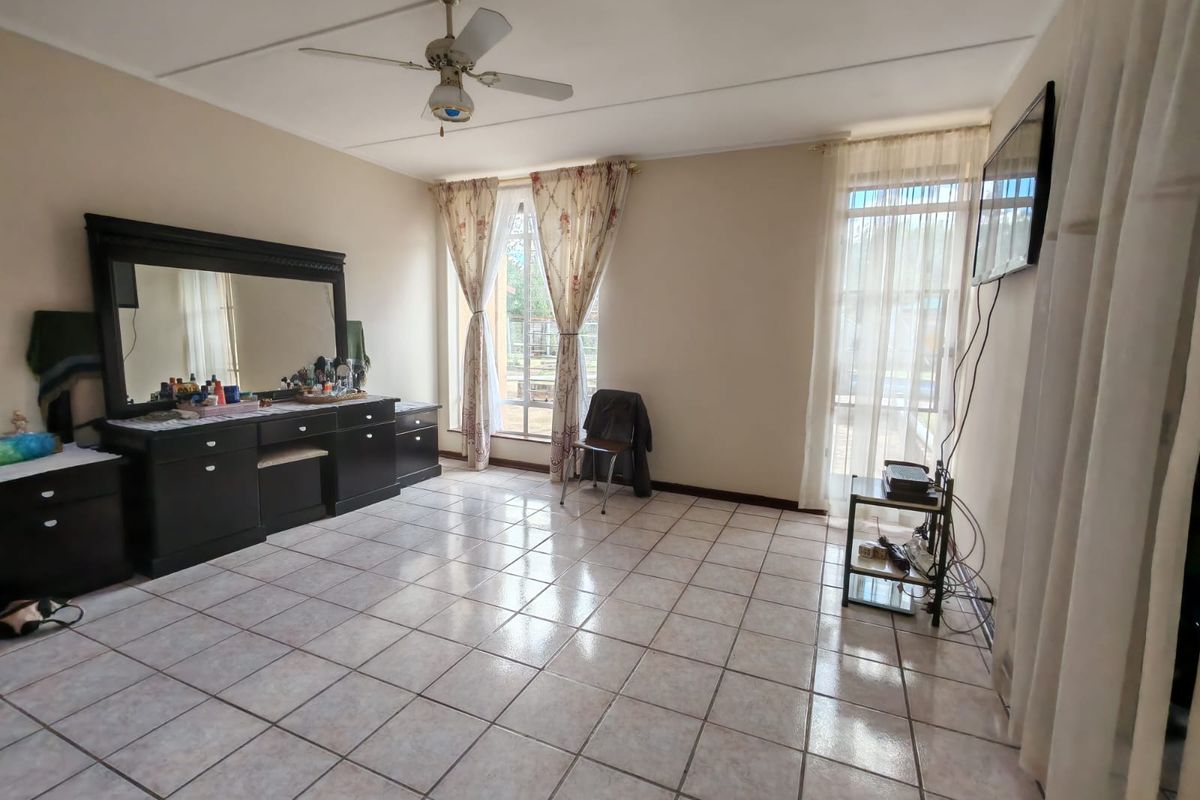 A spacious bedroom featuring neutral tiled flooring, a ceiling fan, and large windows that provide ample natural light.