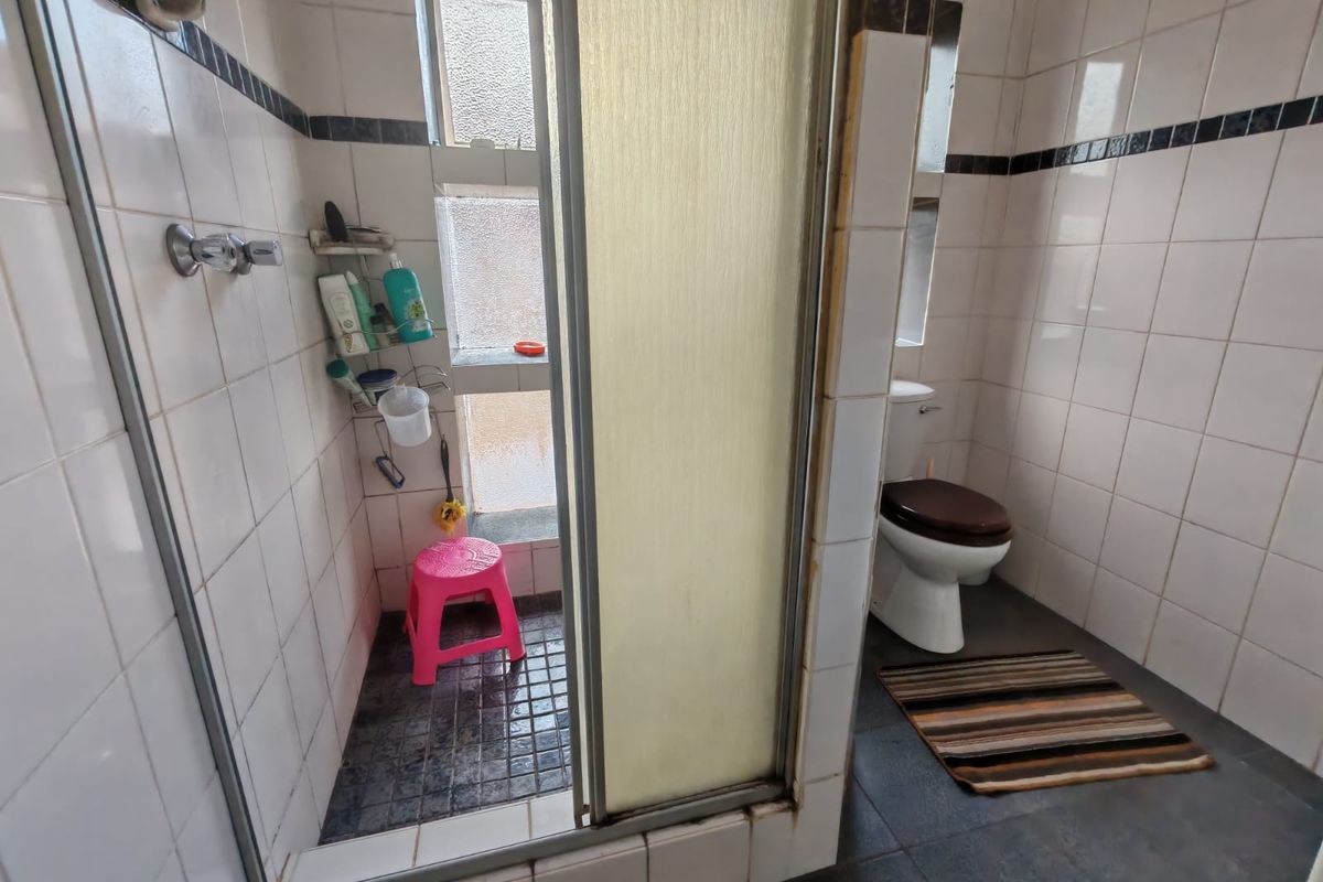 A functional bathroom featuring a shower enclosure and toilet with tiled finishes, presenting an opportunity for modernization and cosmetic updates.