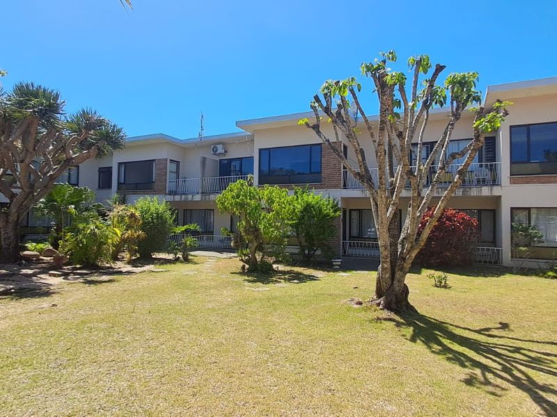 Rear view of the apartment complex featuring a well-maintained garden, private balconies, and large windows providing natural light to the units.