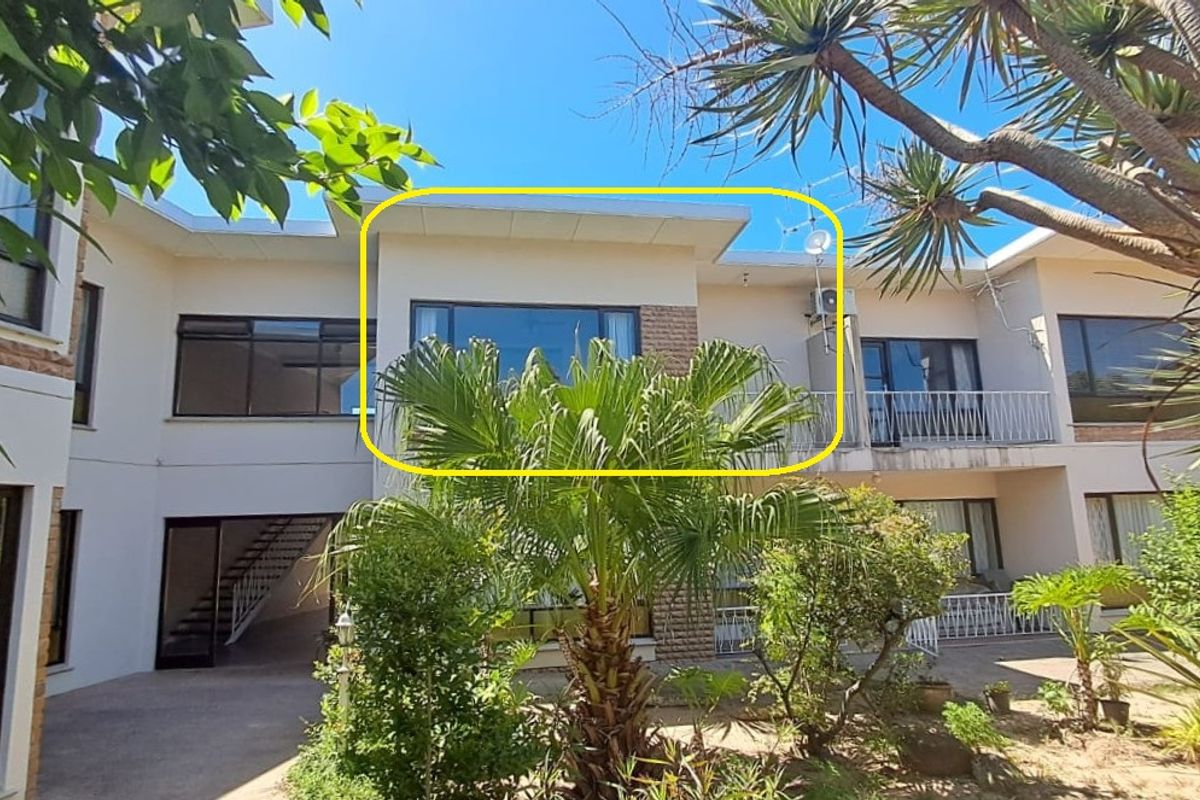 Rear view of the apartment complex featuring a paved courtyard, balcony access, and established garden landscaping.