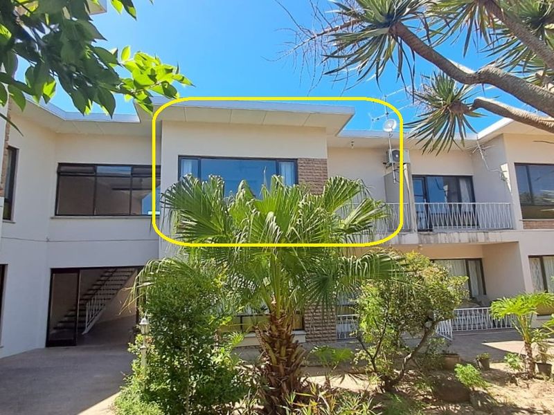 Rear view of the apartment complex featuring a paved courtyard, balcony access, and established garden landscaping.