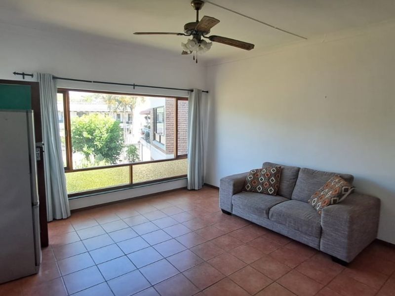 A living room featuring tiled flooring, a ceiling fan, and a large window providing natural light and exterior views.