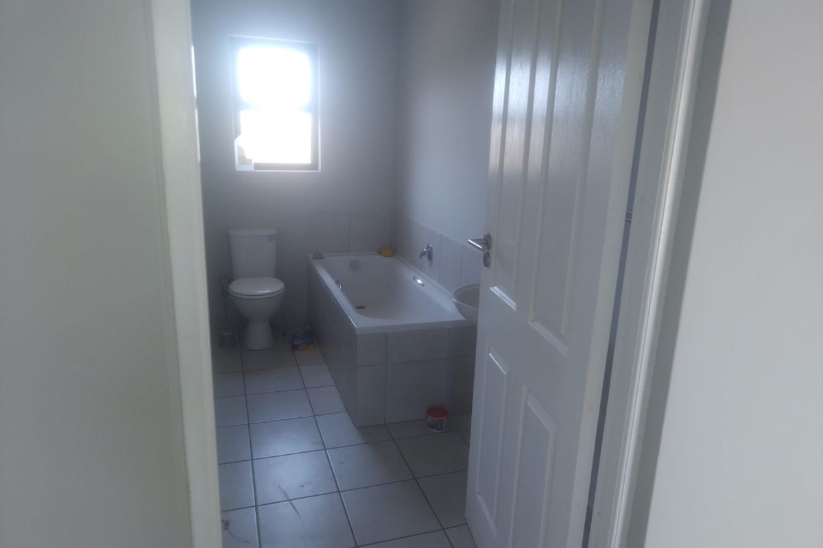 A functional bathroom featuring a built-in bathtub, toilet, and tiled flooring, viewed from the doorway.