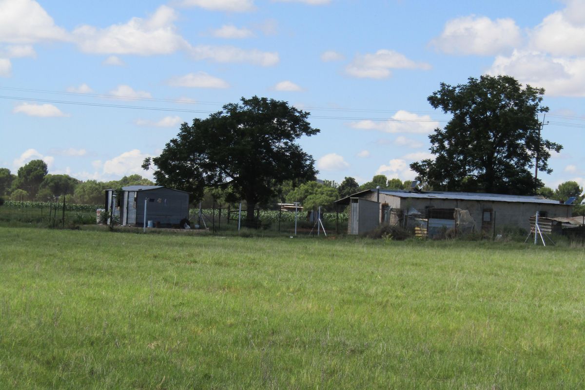 A wide view of the small holding property featuring basic outbuildings and structures set within an expansive open field.