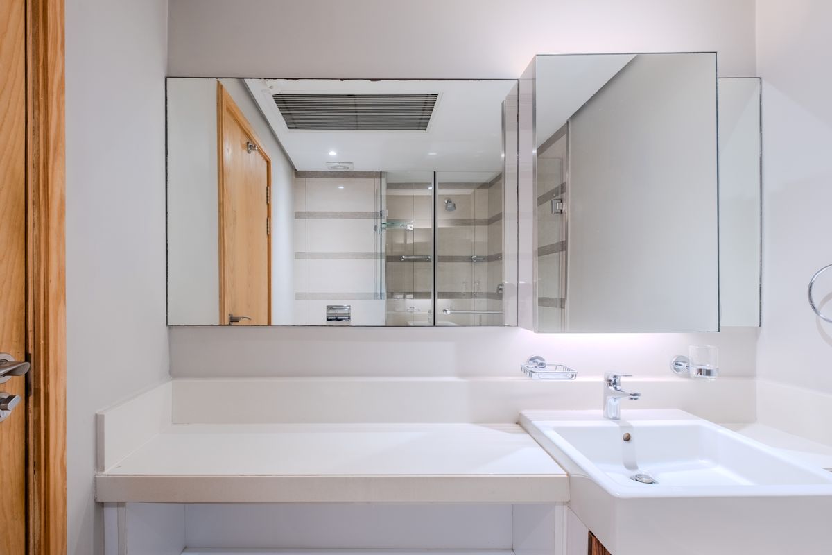 A clean bathroom featuring a vanity countertop with an integrated sink, large wall-mounted mirror, and a tiled shower enclosure with glass doors.