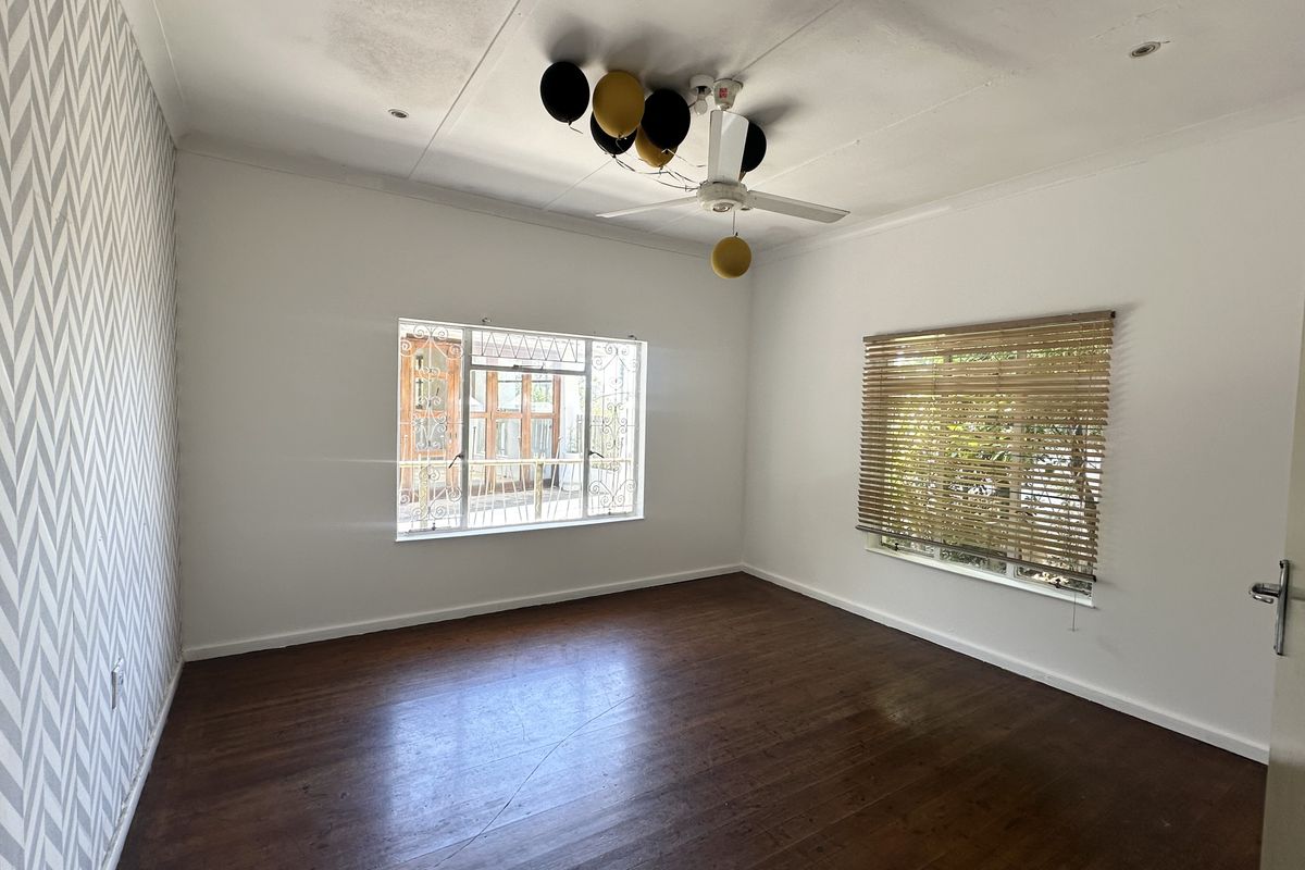 A vacant bedroom featuring timber flooring, a ceiling fan, and security bars on the windows, with some visible water staining on the ceiling.