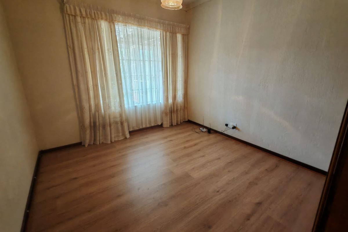 A vacant bedroom featuring wood-look laminate flooring, a large window with curtains, and a central pendant light fixture.