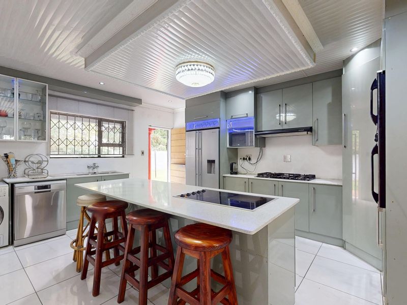 Modern kitchen featuring a central island with quartz countertops, built-in gas hob, integrated appliances, and ample cabinetry, finished with sleek tiled flooring.