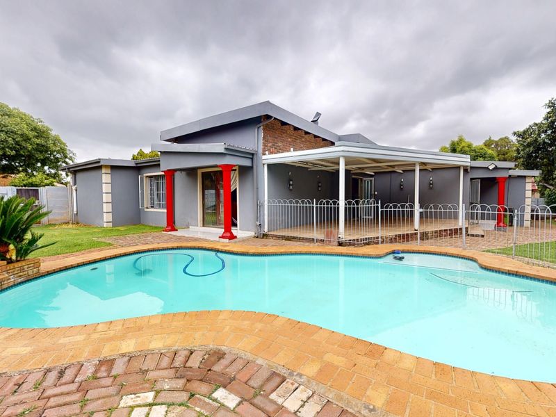 Rear exterior view featuring a swimming pool with brick paving, a covered patio area, and metal perimeter fencing.